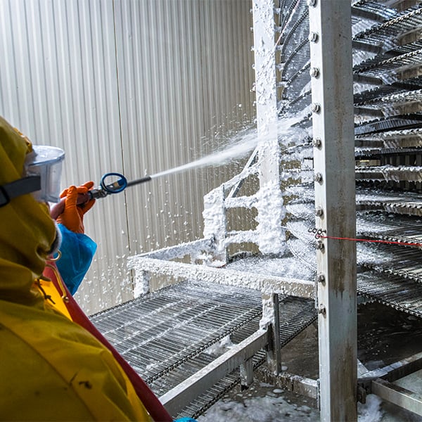 employee spraying foam on facility equipment