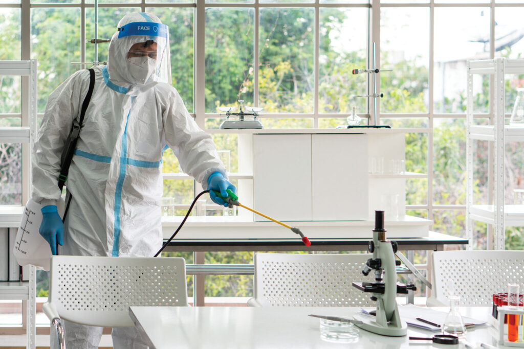 man in sterilized equipment spraying lab surfaces