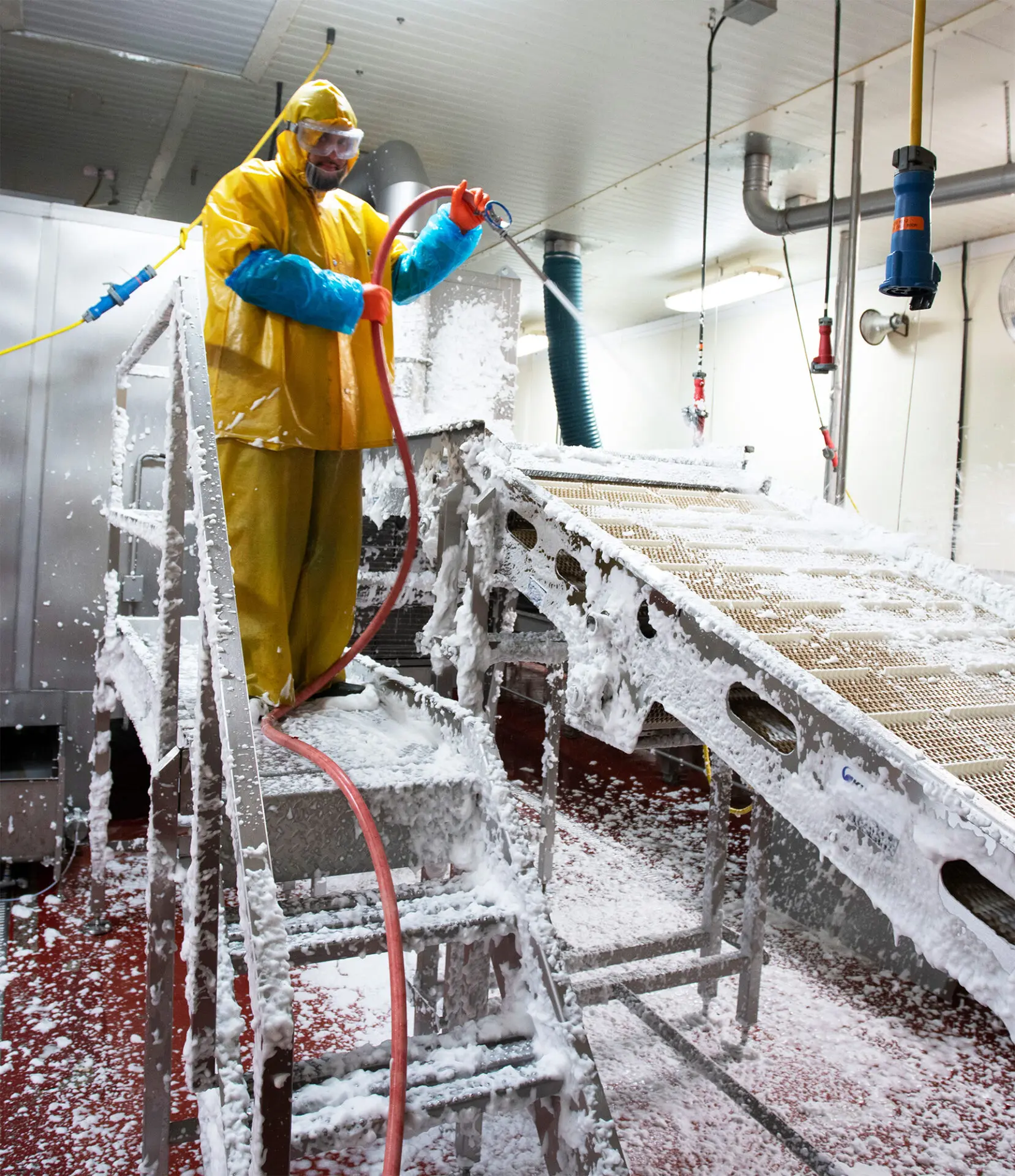man wearing ppe spraying foam in food conveyor facility